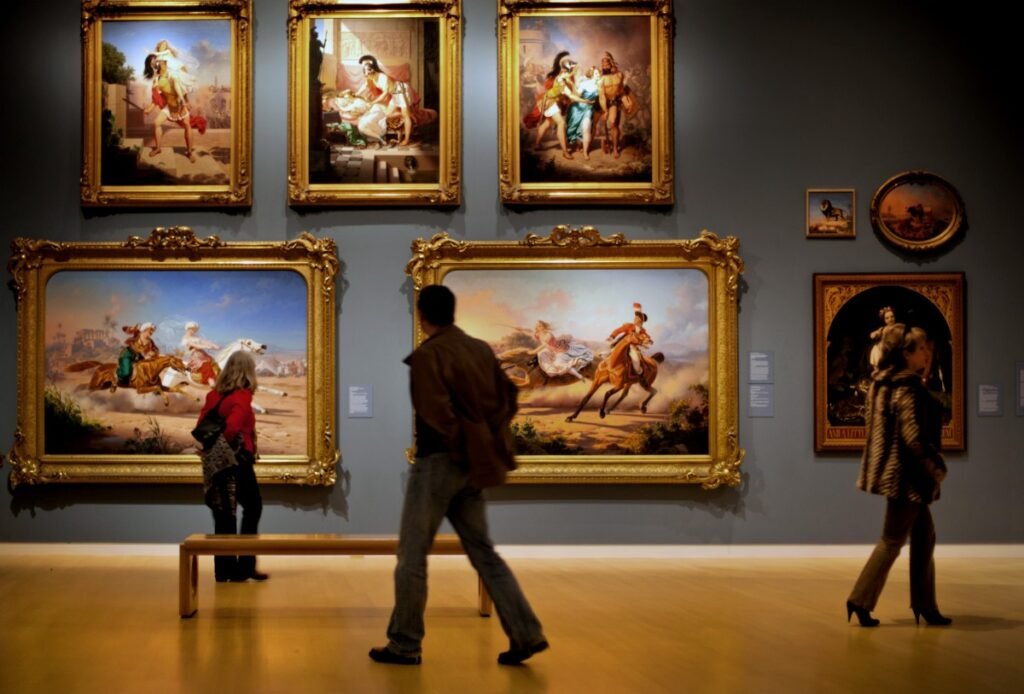 A museum with paintings on the wall in two rows. Shadowy indistinct people are in front of them